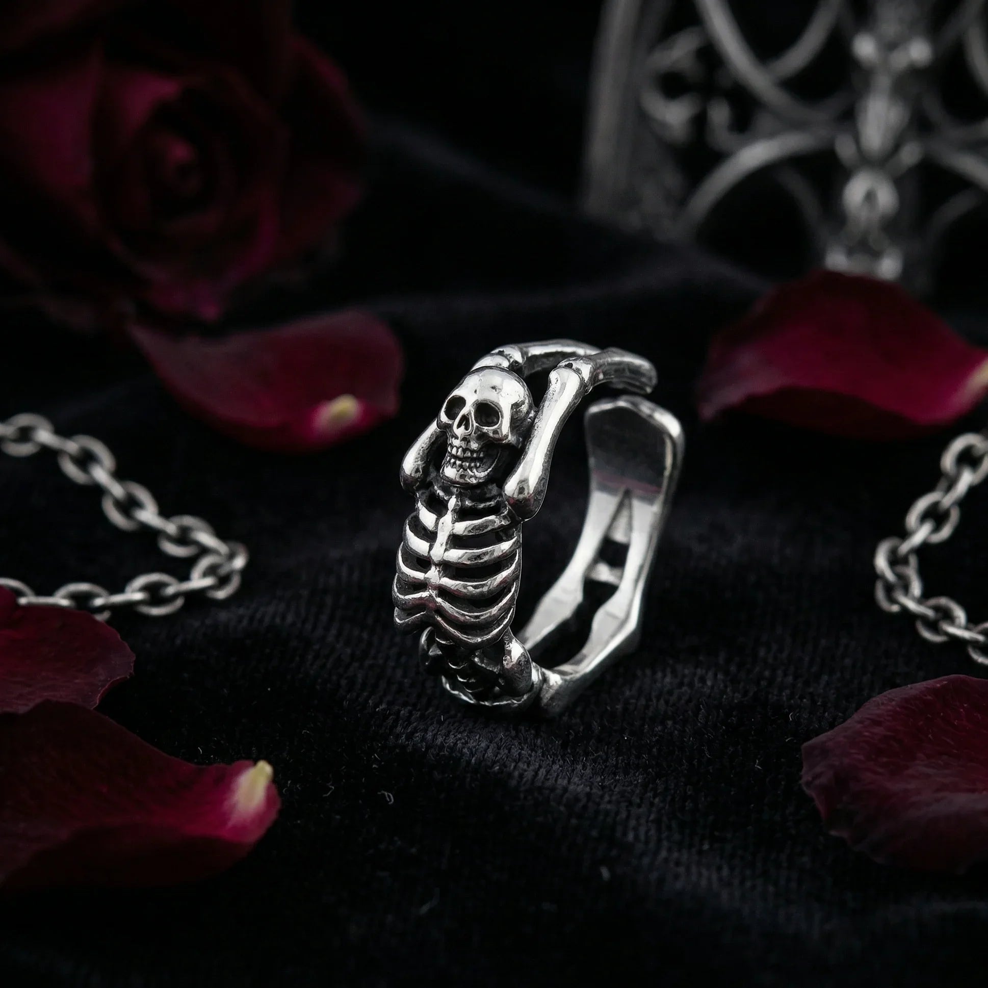 Close-up of Vamp Romantic adjustable skeleton ring with detailed skull and spine design, surrounded by black velvet and red rose petals – tarnish-resistant gothic jewelry