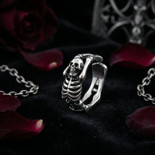 Close-up of Vamp Romantic adjustable skeleton ring with detailed skull and spine design, surrounded by black velvet and red rose petals – tarnish-resistant gothic jewelry