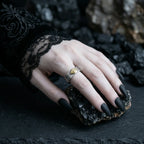 Hand with black nail polish wearing a gold ring on a dark stone surface