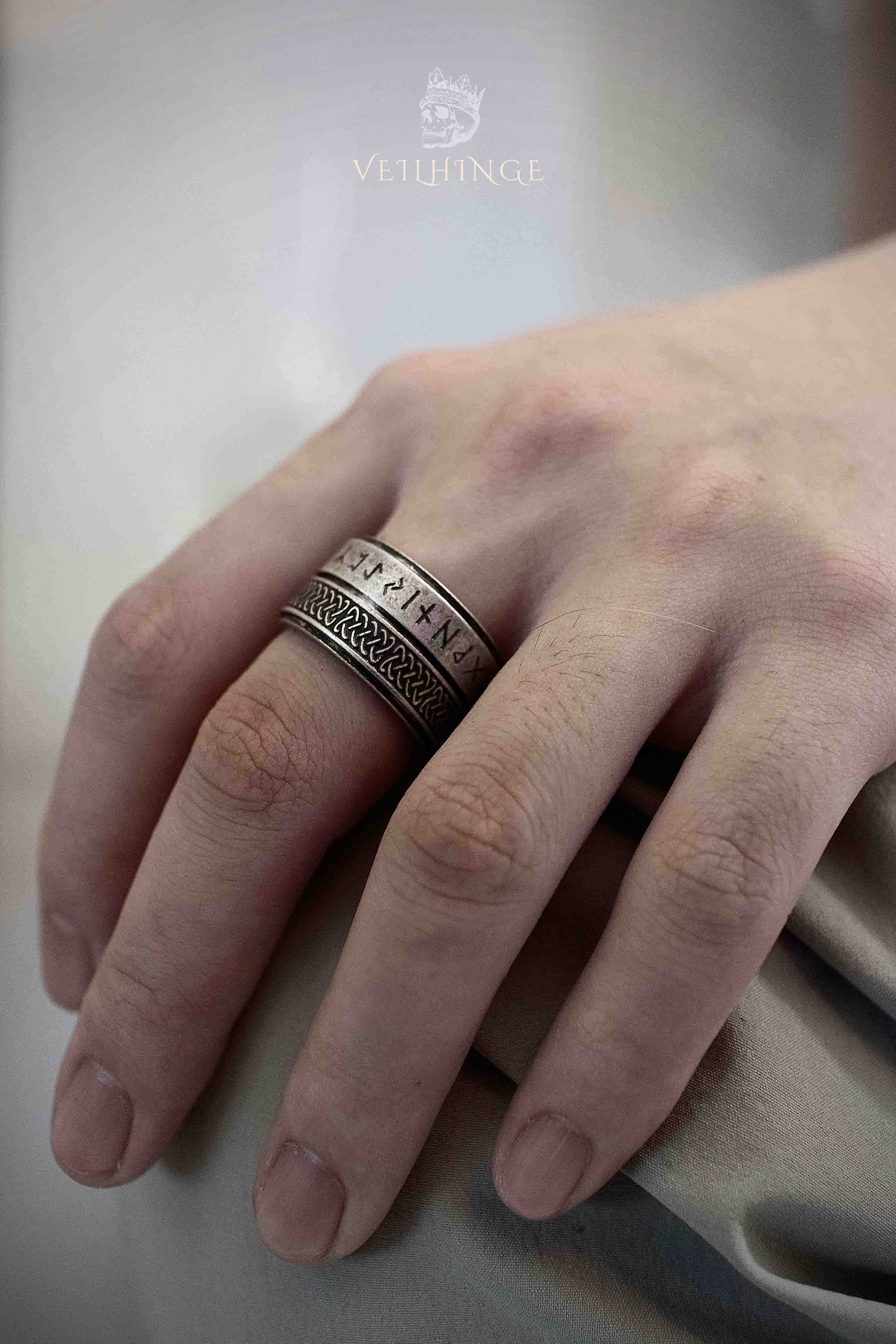 Double-layer spinner ring worn on a middle finger, rotating Elder Futhark rune band above a spinning Celtic braid band, wide oxidized silver ring with two independently moving layers