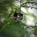 Viking rune ring with transparent resin inlay and Triquetra symbol resting on a pine branch, Celtic border along both edges in oxidized silver