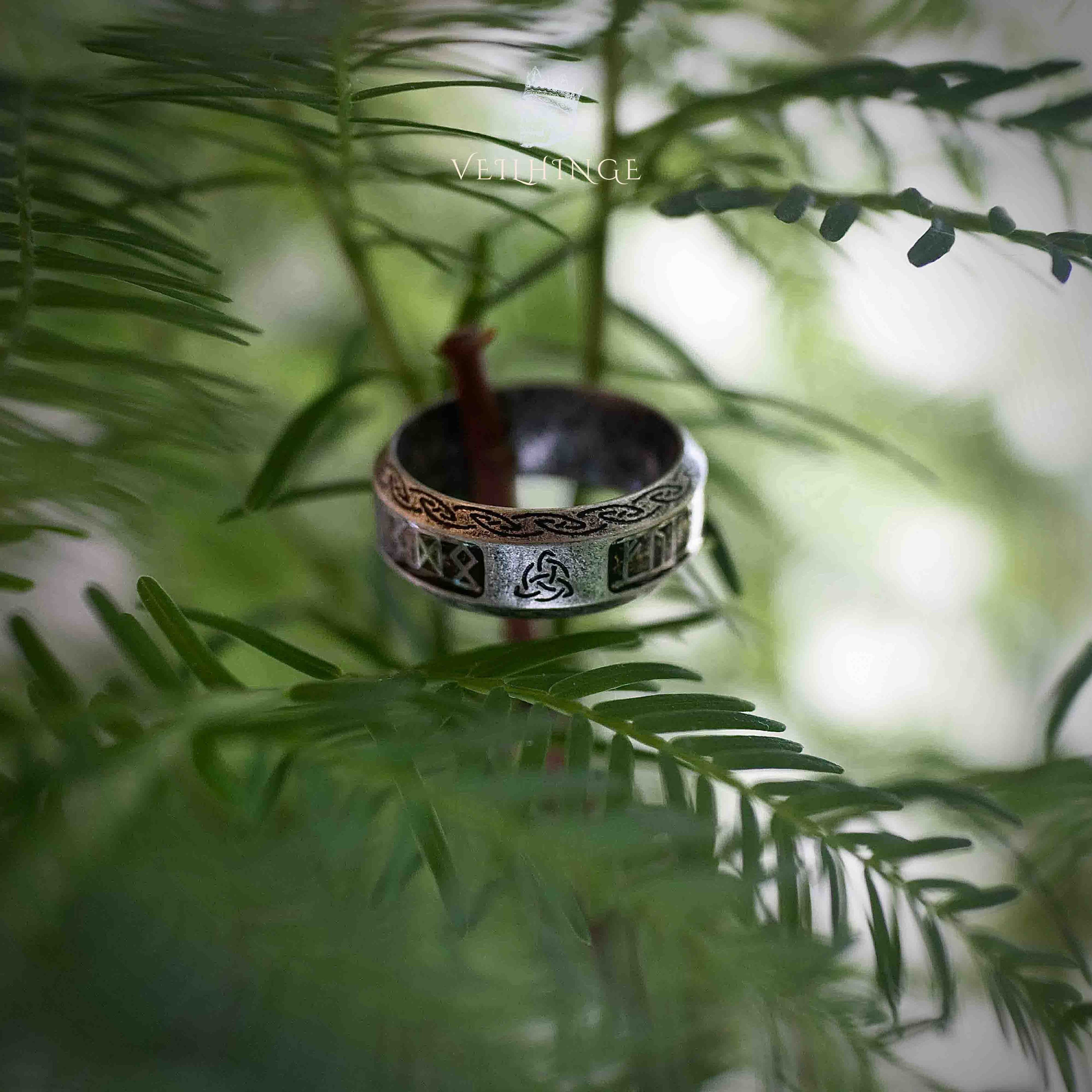 Viking rune ring with transparent resin inlay and Triquetra symbol resting on a pine branch, Celtic border along both edges in oxidized silver