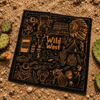Black bandana laid flat on desert sand showing gold line-art icons including a cowboy hat, Native American headdress, cactus, revolver, and skull with the text Wild West at the center