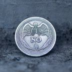 Close-up of the YES face of a decision coin engraved with two raised hands, sun and crescent moon above, all-seeing eye below, on dark stone surface