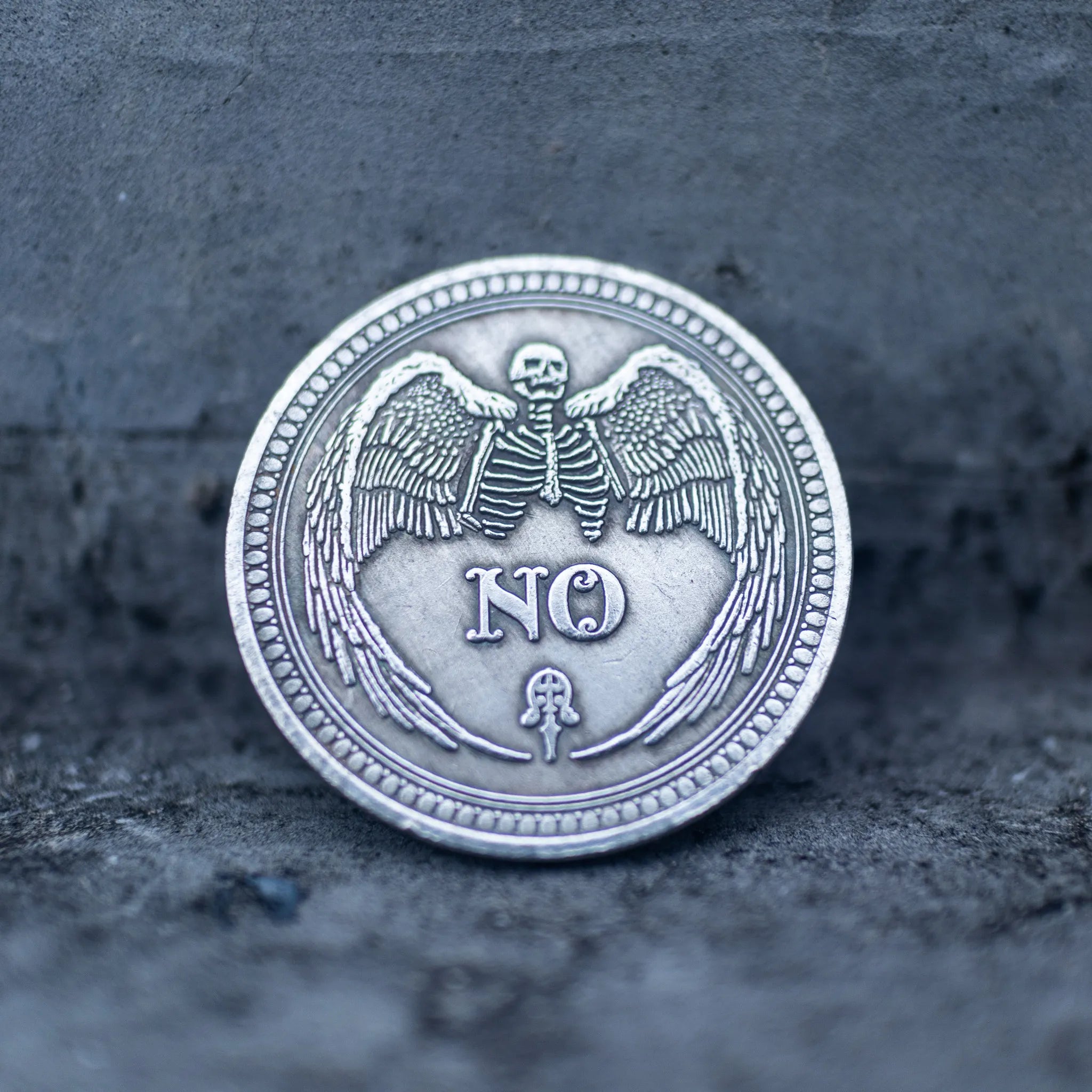 Close-up of the YES face of a decision coin engraved with two raised hands, sun and crescent moon above, all-seeing eye below, on dark stone surface
