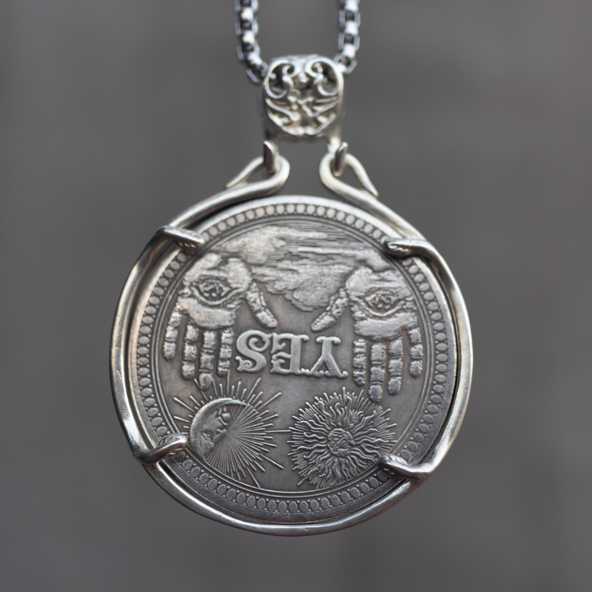 Decision coin pendant reversed to the YES side showing two raised hands, sun, crescent moon, and all-seeing eye motifs, held in a four-prong bezel on a box chain