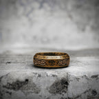 Antique gold Viking ring resting on a stone surface, engraved with a Yggdrasil tree of life and Celtic knotwork pattern along the band

