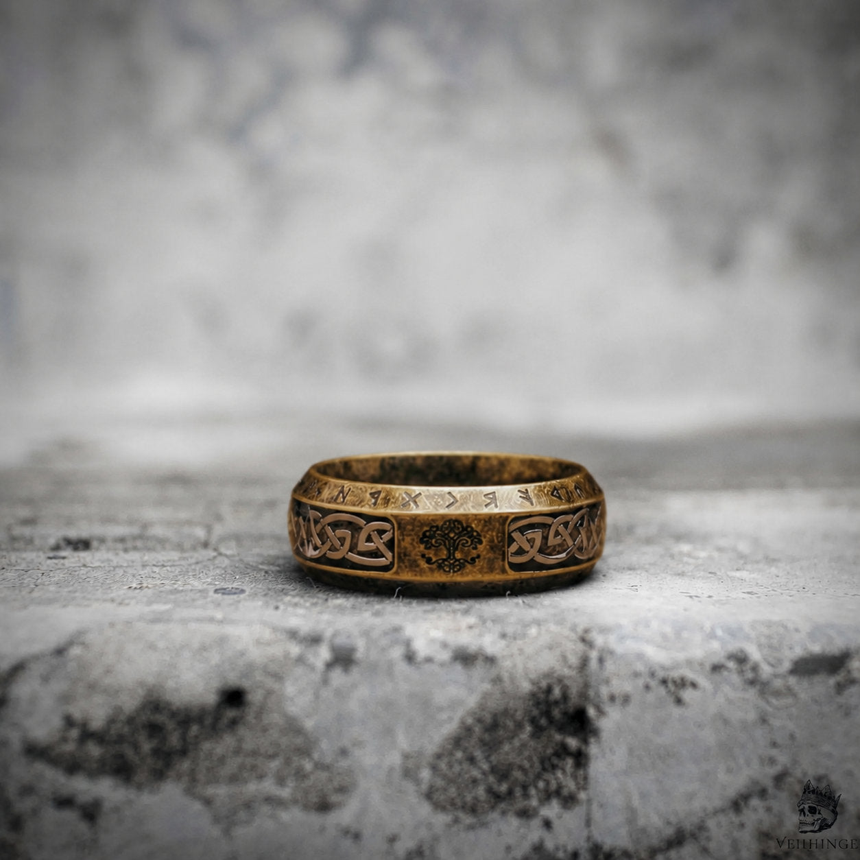Antique gold Viking ring resting on a stone surface, engraved with a Yggdrasil tree of life and Celtic knotwork pattern along the band

