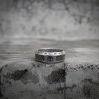 Antique silver Viking ring placed on a concrete ledge, featuring Norse rune engravings and a tree of life motif carved around the band