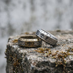 Antique gold and antique silver Yggdrasil Viking rings placed side by side on a mossy stone, showing both colorways together in a natural outdoor setting